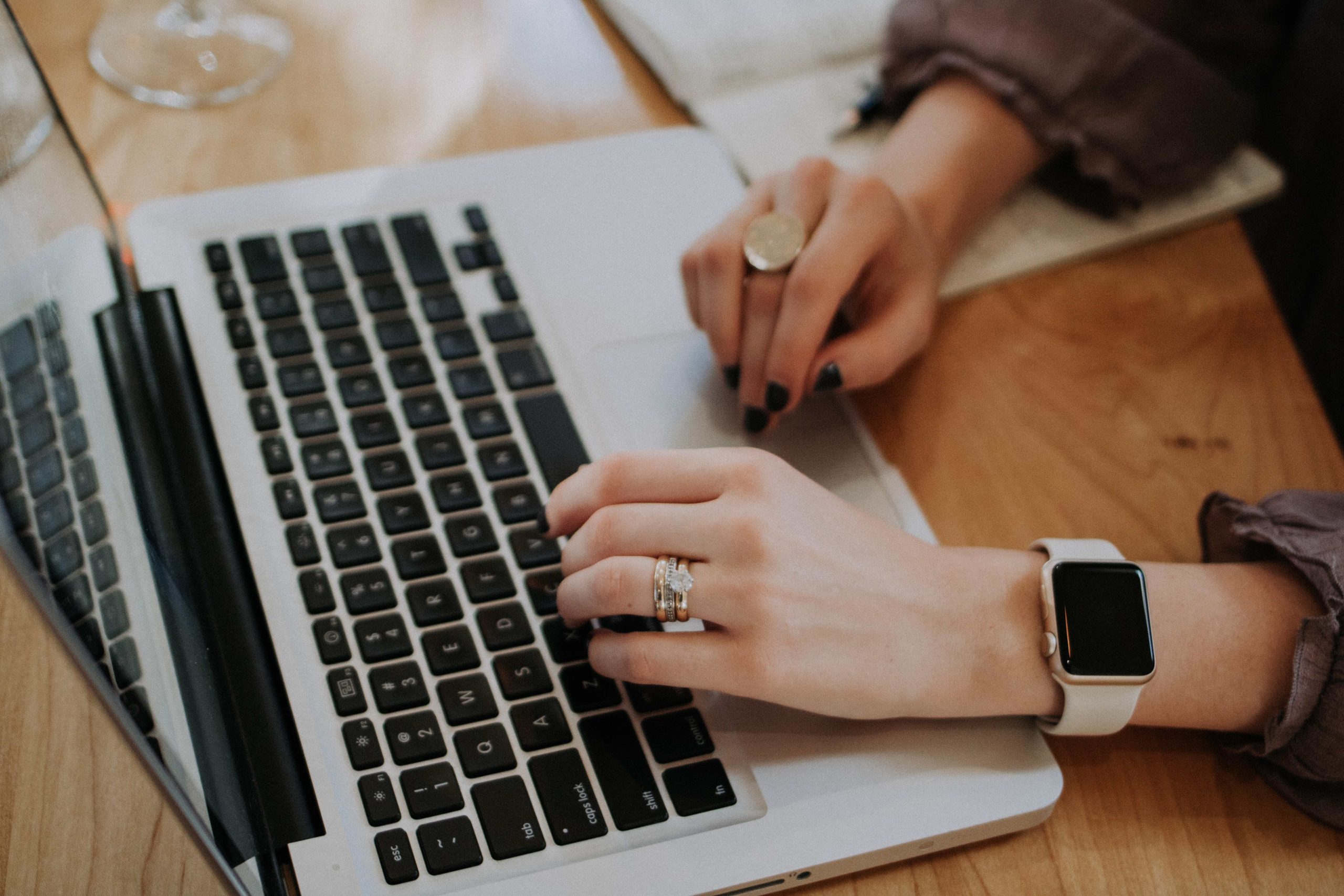 A woman wearing a smartwatch and typing on her laptop.