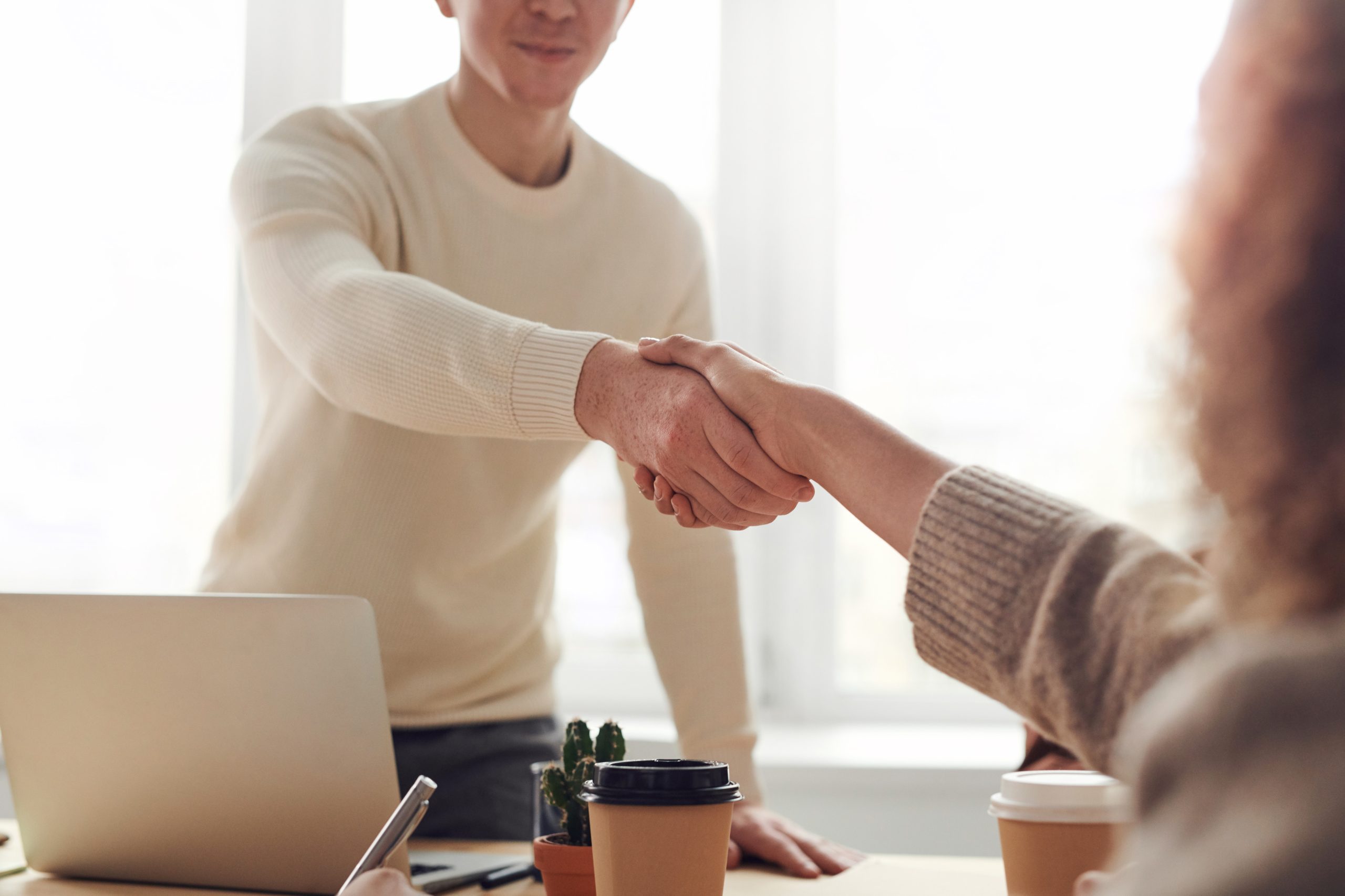 Two people shaking hands over a desk.