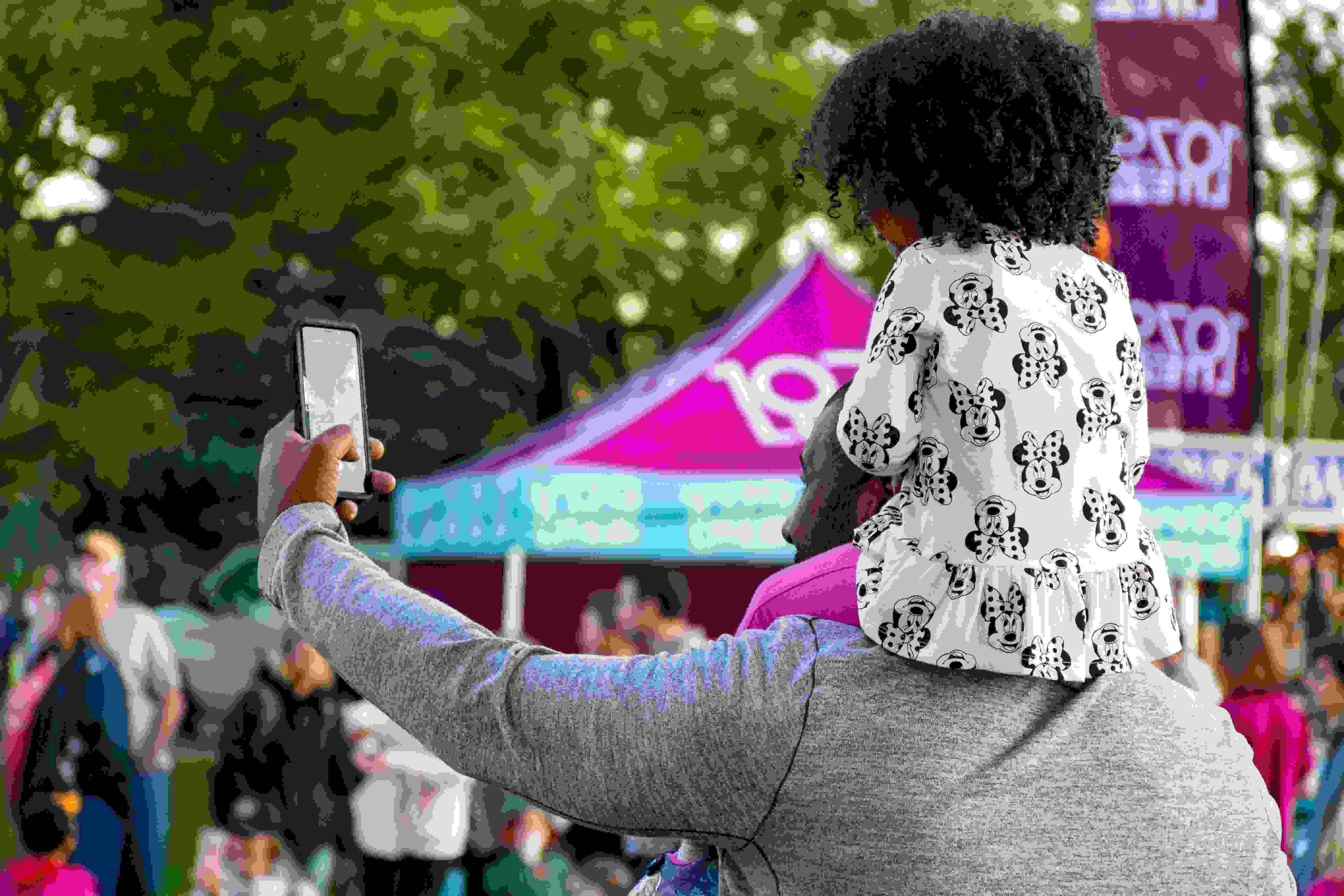 An image of a father taking a selfie at a local charity event with his daughter on his shoulders.