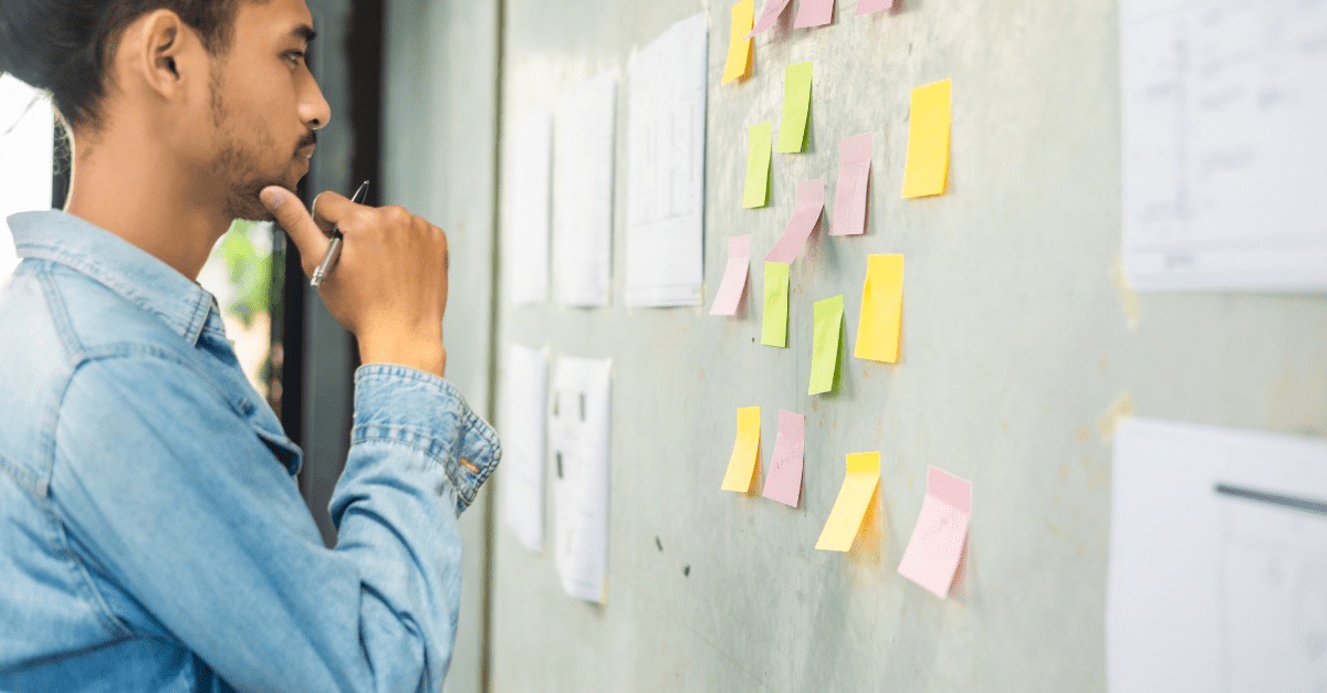 A man examining a whiteboard of sticky notes.